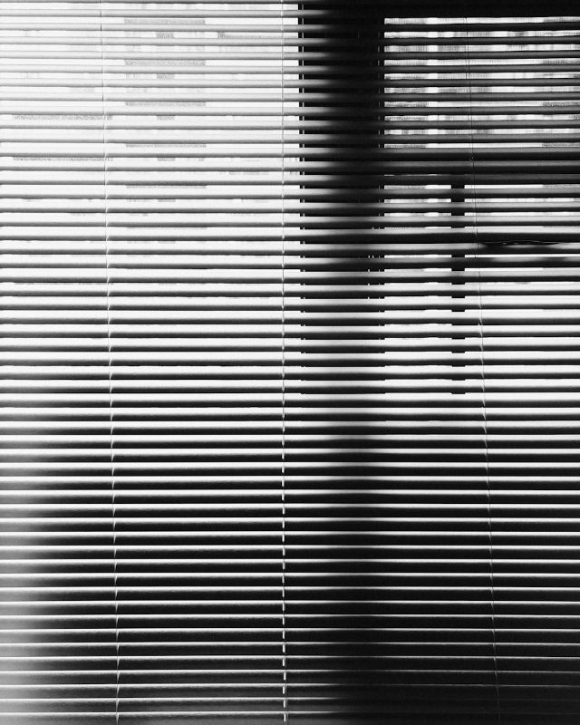 Close view of white slatted blinds with daylight behind them